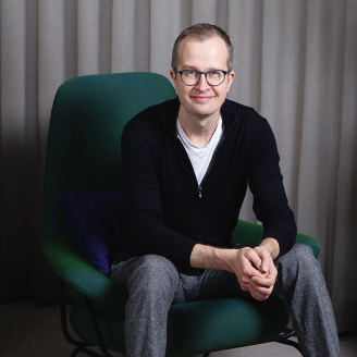 A picture of smiling Tommi Vilkamo, Director at RELEX labs sitting on a green chair.