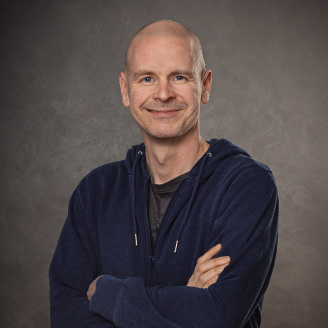 A picture of smiling Tero Hottinen, Head of Strategic Technology Partnerships at Kone in a navy blue hoodie against a gray background.