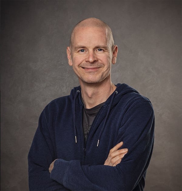 A picture of smiling Tero Hottinen, Head of Strategic Technology Partnerships at Kone in a navy blue hoodie against a gray background.