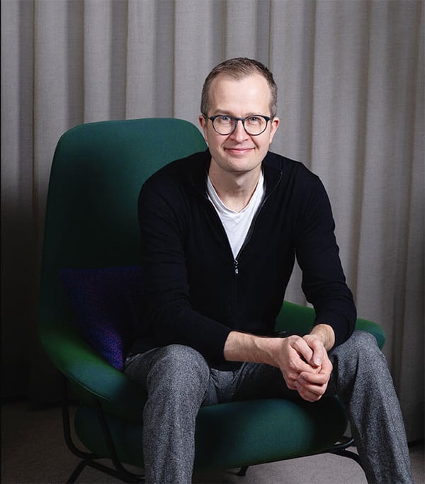 A picture of smiling Tommi Vilkamo, Director at RELEX labs sitting on a green chair.